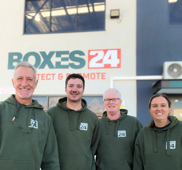 Four people wearing green hoodies with 'Boxes24' logo in front of a company vehicle.