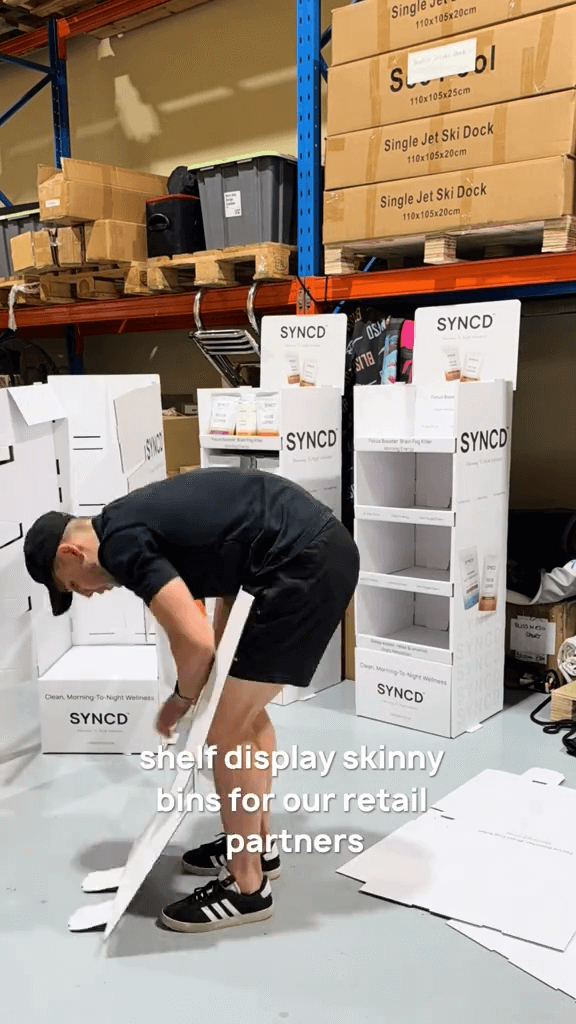 Person arranging 'SYNCD' shelf display bins in a warehouse setting.