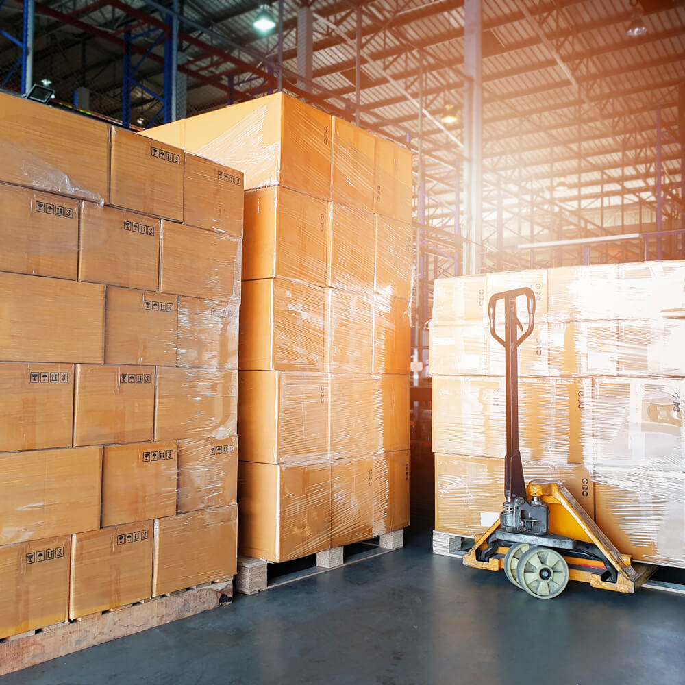 Stacks of cardboard boxes in a warehouse with a forklift.