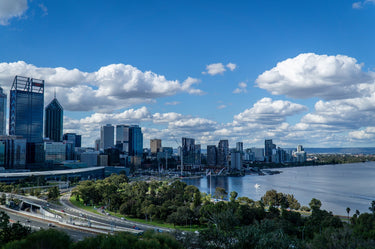 City skyline with buildings and a body of water under a blue sky with clouds.